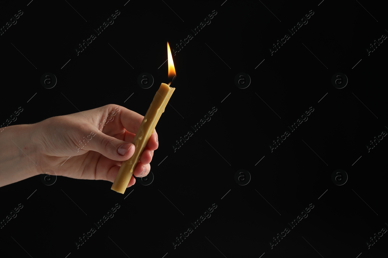 Photo of Woman holding burning church candle on black background, closeup. Space for text