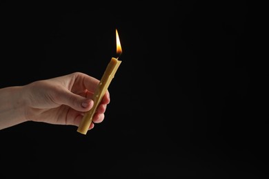 Woman holding burning church candle on black background, closeup. Space for text