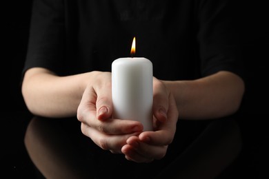 Woman holding burning candle on black background, closeup