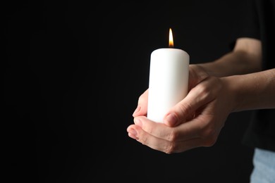 Photo of Woman holding burning candle on black background, closeup. Space for text