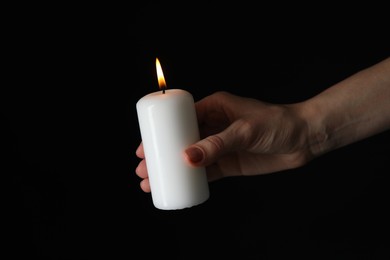 Photo of Woman holding burning candle on black background, closeup