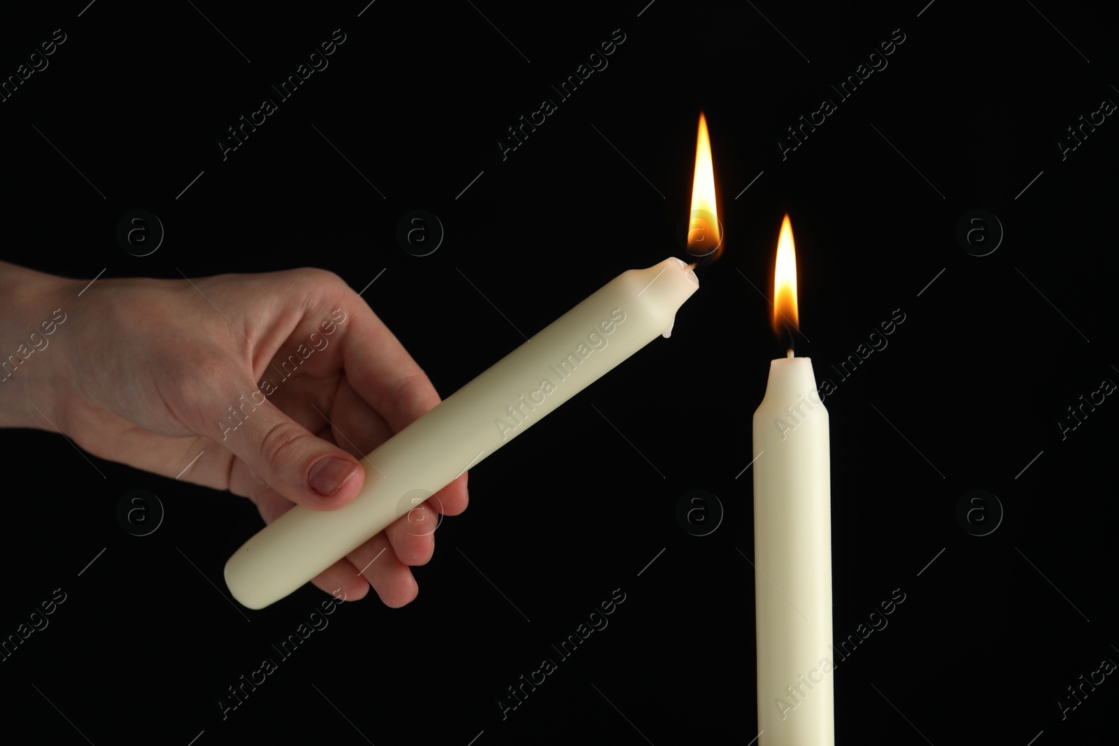 Photo of Woman lighting candle on black background, closeup