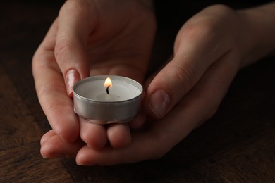 Woman holding burning tealight candle at wooden table, closeup