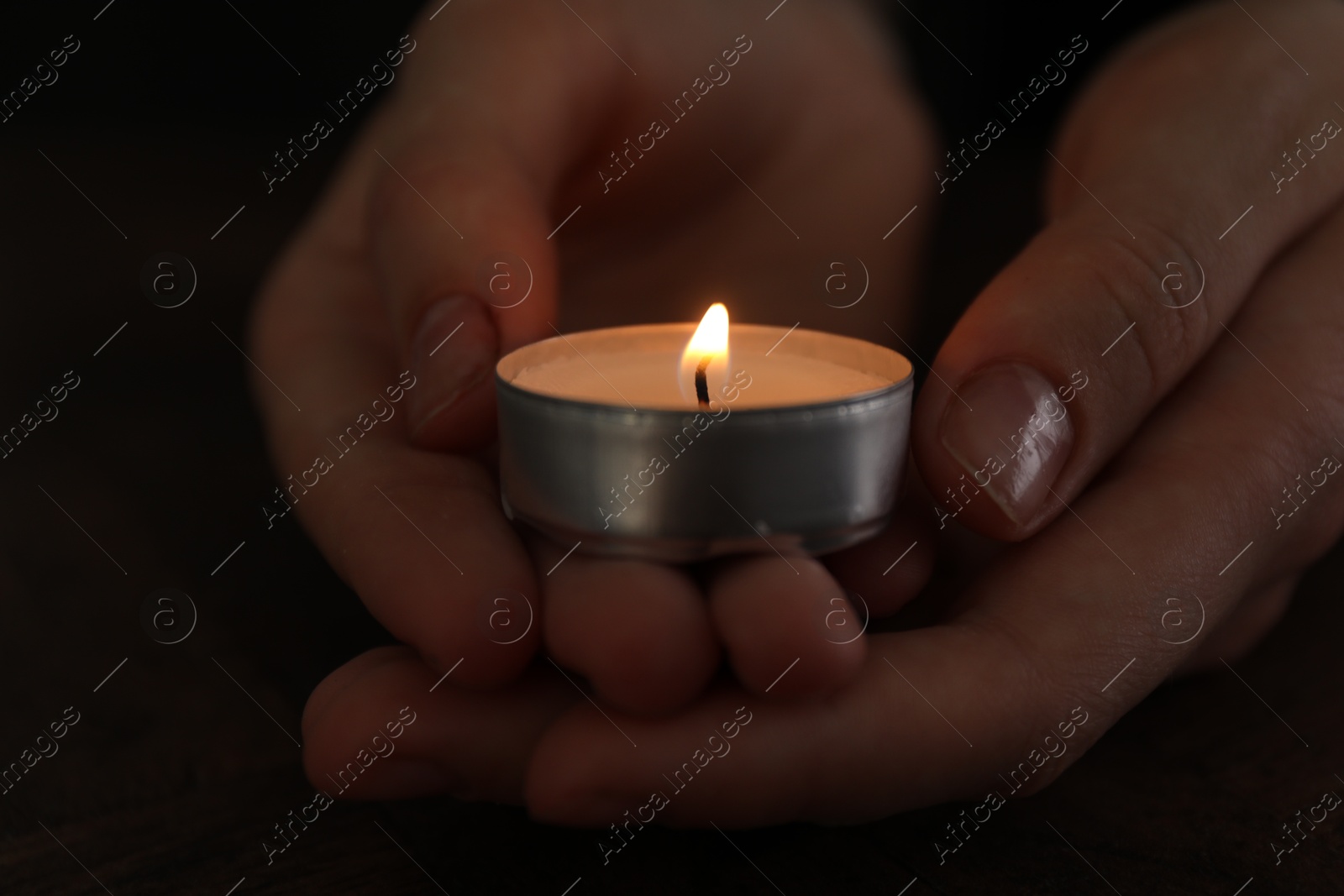 Photo of Woman holding burning tealight candle on black background, closeup