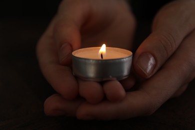 Photo of Woman holding burning tealight candle on black background, closeup