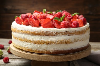 Tasty sponge cake with fresh berries and mint on wooden table, closeup