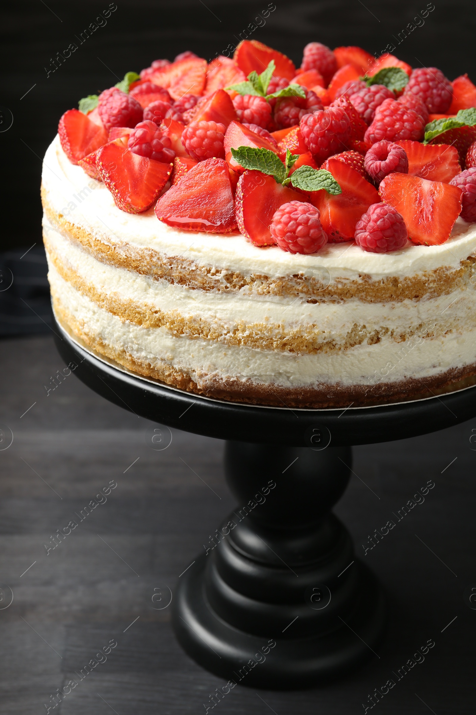 Photo of Tasty sponge cake with fresh berries and mint on dark gray wooden table, closeup