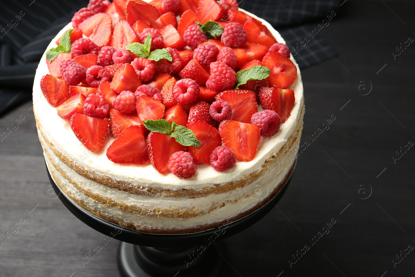 Photo of Tasty sponge cake with fresh berries and mint on dark gray table, closeup