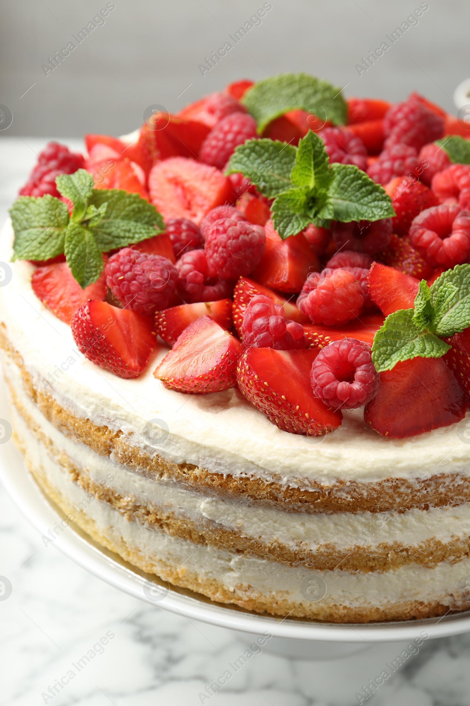 Photo of Tasty sponge cake with fresh berries and mint on white marble table, closeup