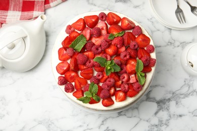 Photo of Tasty sponge cake with fresh berries and teapot on white marble table, flat lay