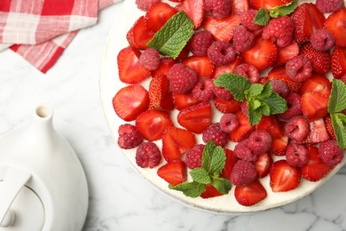 Photo of Tasty sponge cake with fresh berries and teapot on white marble table, flat lay