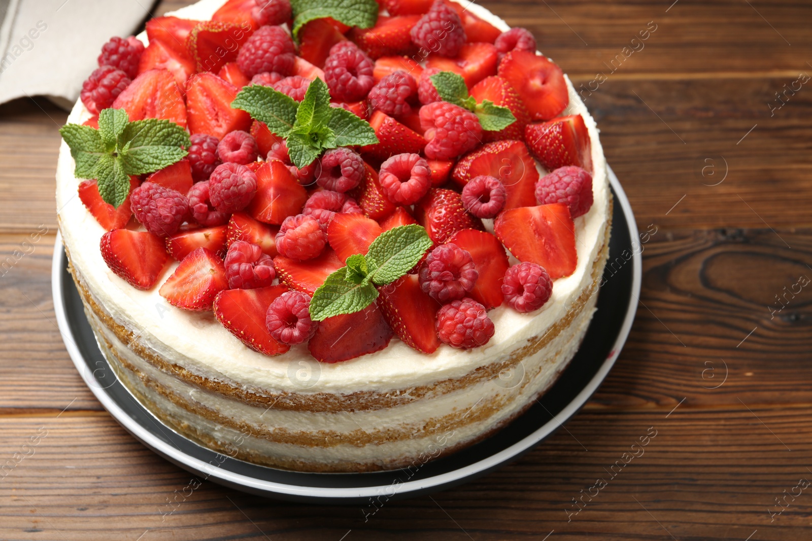 Photo of Tasty sponge cake with fresh berries and mint on wooden table, closeup