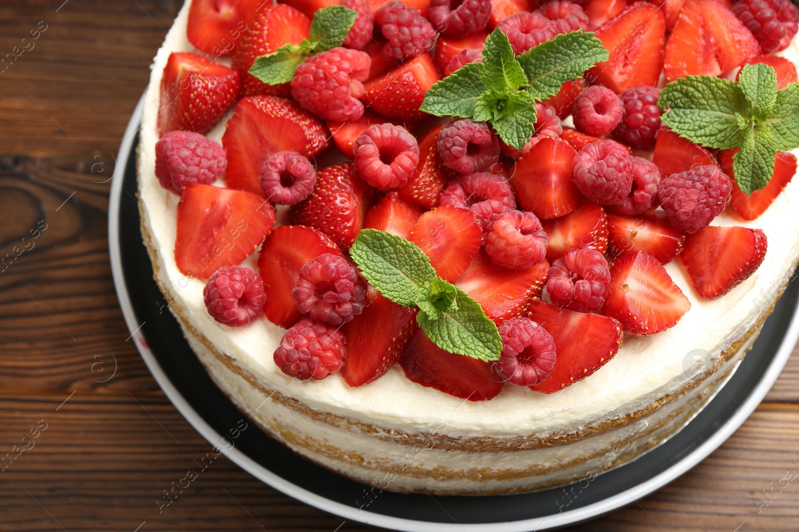 Photo of Tasty sponge cake with fresh berries and mint on wooden table, closeup