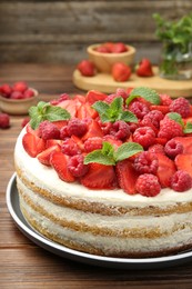 Tasty sponge cake with fresh berries and mint on wooden table, closeup