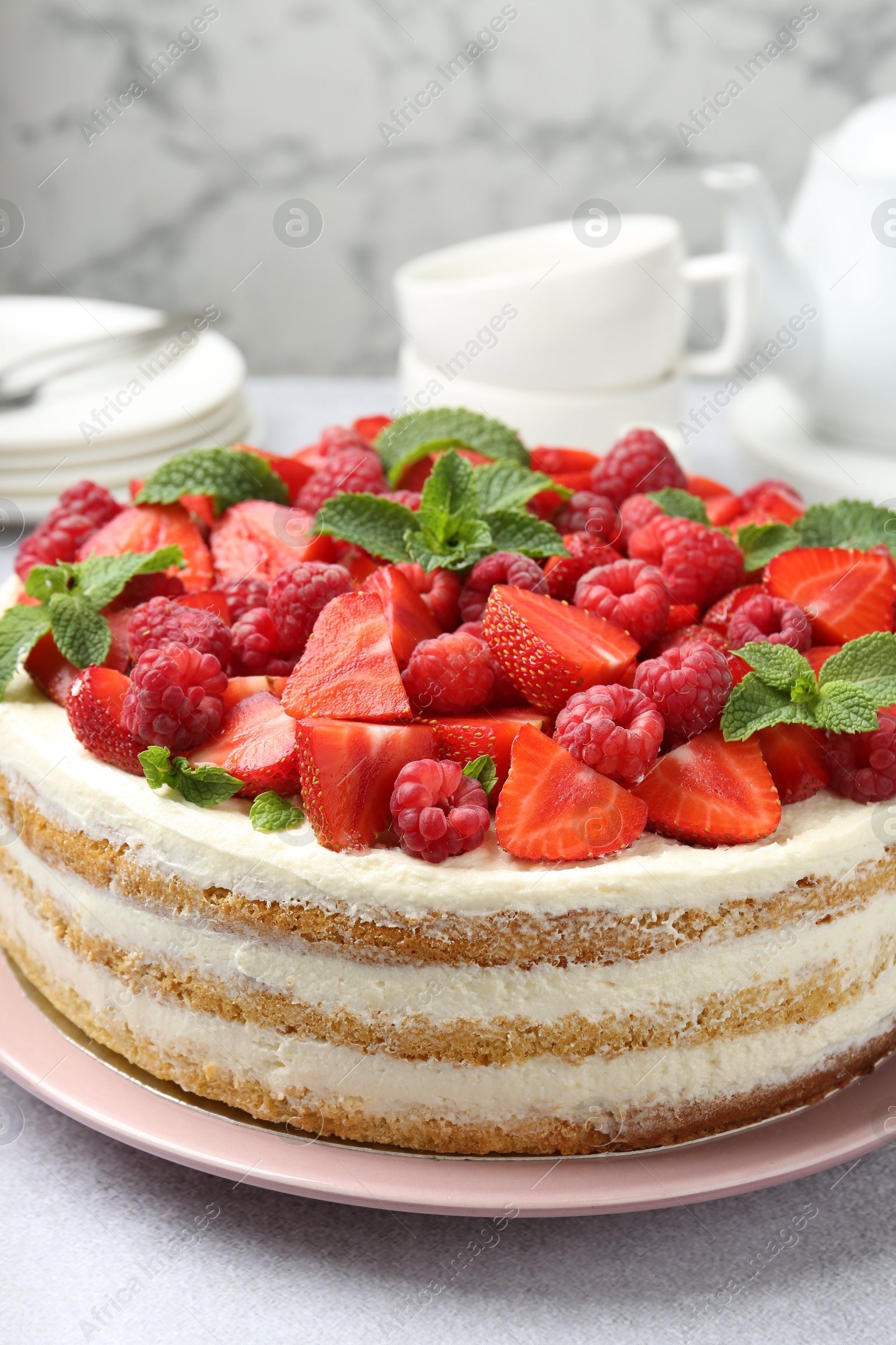 Photo of Tasty sponge cake with fresh berries and mint on light gray table, closeup