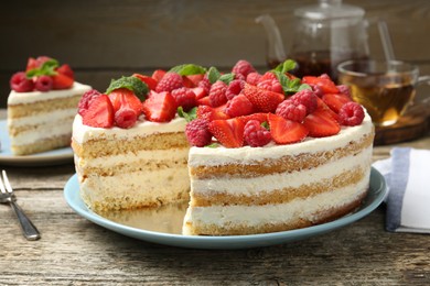 Photo of Tasty sponge cake with fresh berries and mint on wooden table, closeup