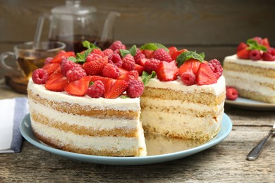 Photo of Tasty sponge cake with fresh berries and mint on wooden table, closeup