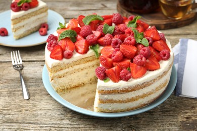 Photo of Tasty sponge cake with fresh berries and mint on wooden table, closeup