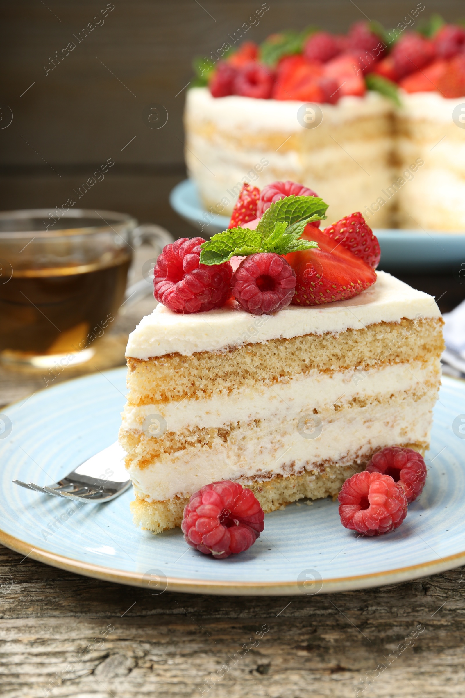 Photo of Piece of tasty sponge cake with fresh berries and mint served on wooden table, closeup