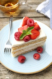 Piece of tasty sponge cake with fresh berries and mint served on wooden table, closeup