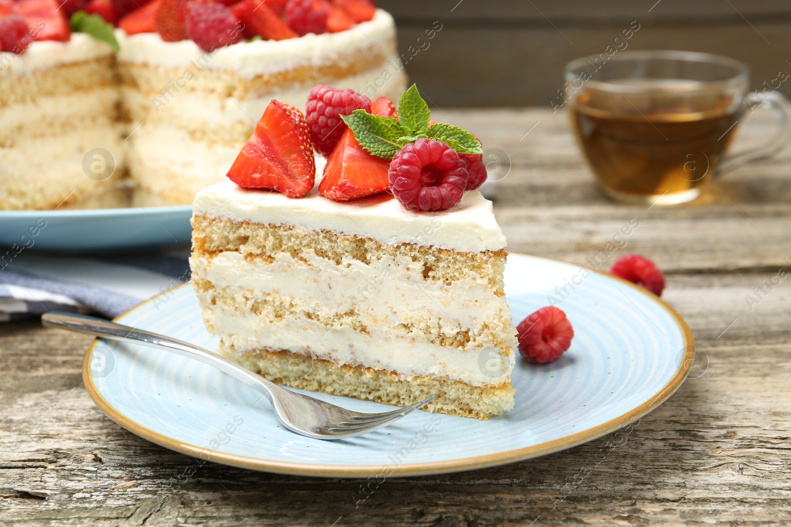 Photo of Piece of tasty sponge cake with fresh berries and mint served on wooden table, closeup