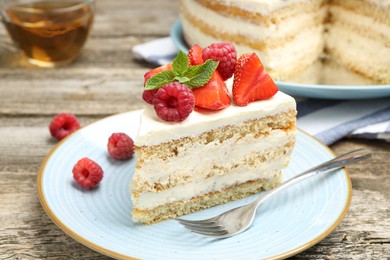 Photo of Piece of tasty sponge cake with fresh berries and mint served on wooden table, closeup