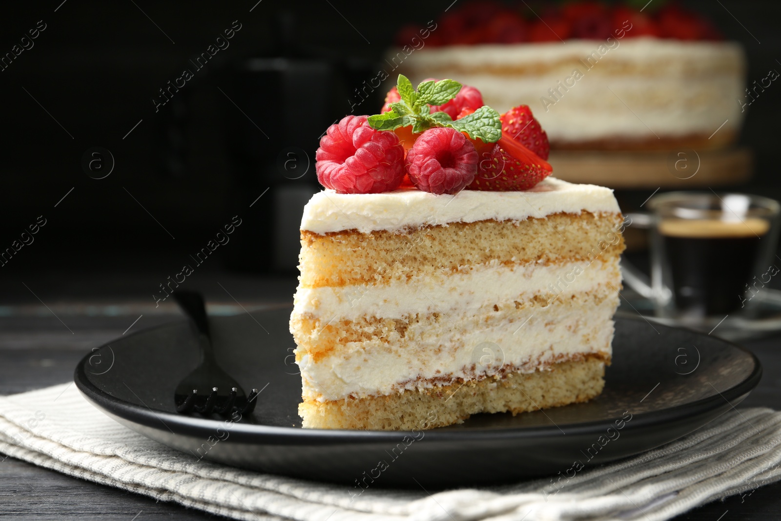 Photo of Piece of tasty sponge cake with fresh berries and mint served on black table, closeup