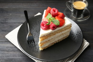 Piece of tasty sponge cake with fresh berries and mint served on black wooden table, closeup