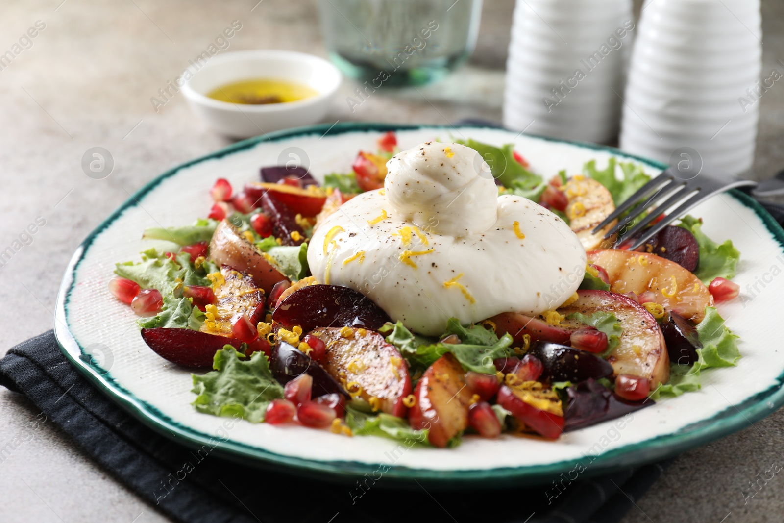 Photo of Plate with fresh burrata salad on grey textured table, closeup