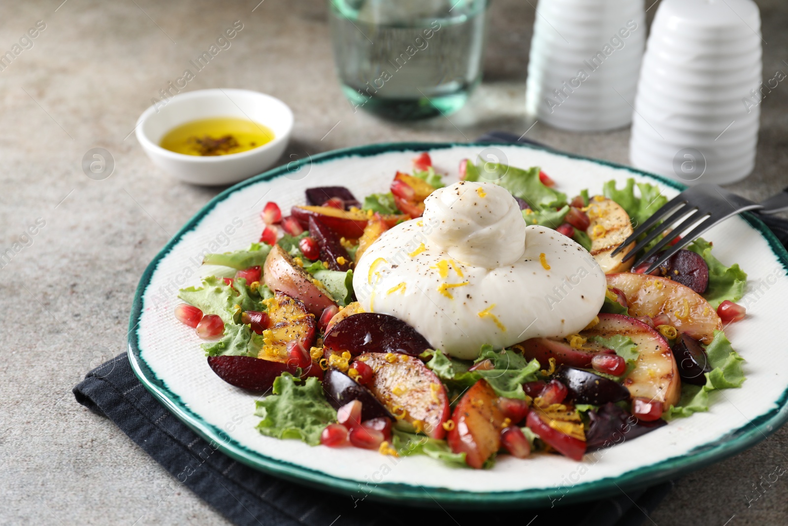 Photo of Plate with fresh burrata salad on grey textured table, closeup