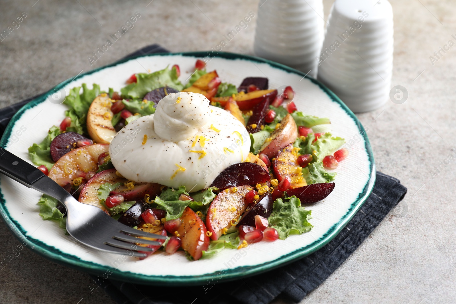 Photo of Plate with fresh burrata salad on grey textured table, closeup