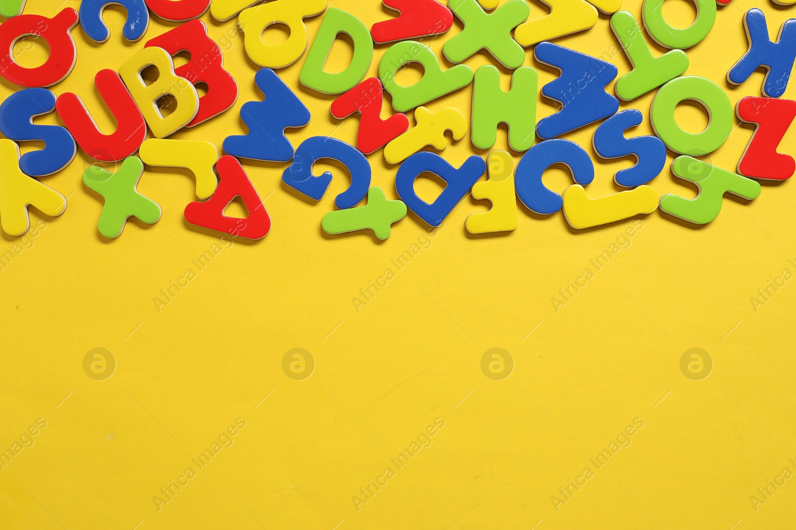 Photo of Learning alphabet. Magnetic letters on yellow background, flat lay. Space for text