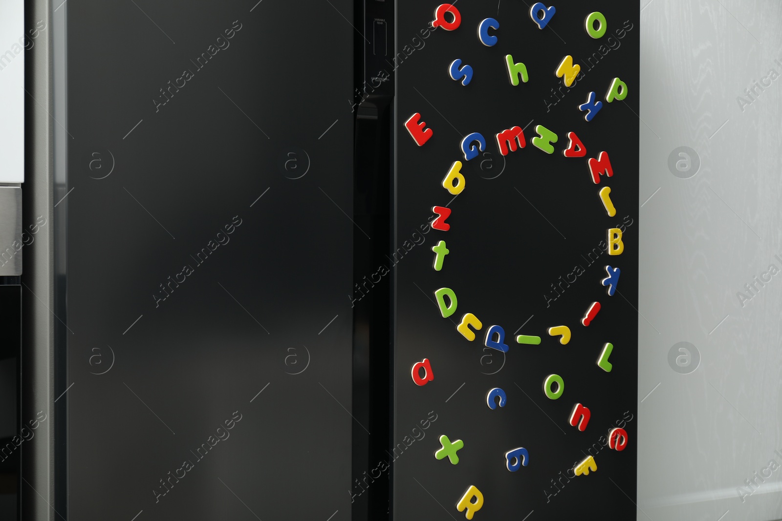 Photo of Many bright magnetic letters on fridge indoors. Learning alphabet