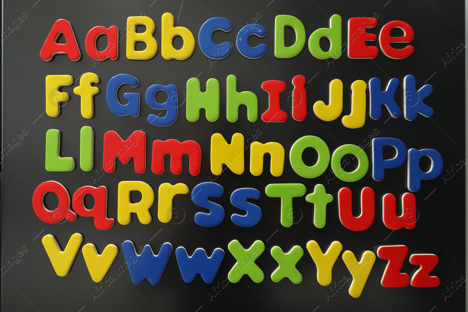 Photo of Alphabetical order. Many bright magnetic letters on fridge