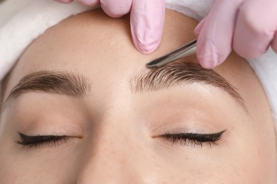 Photo of Beautician plucking young woman's eyebrow, closeup view