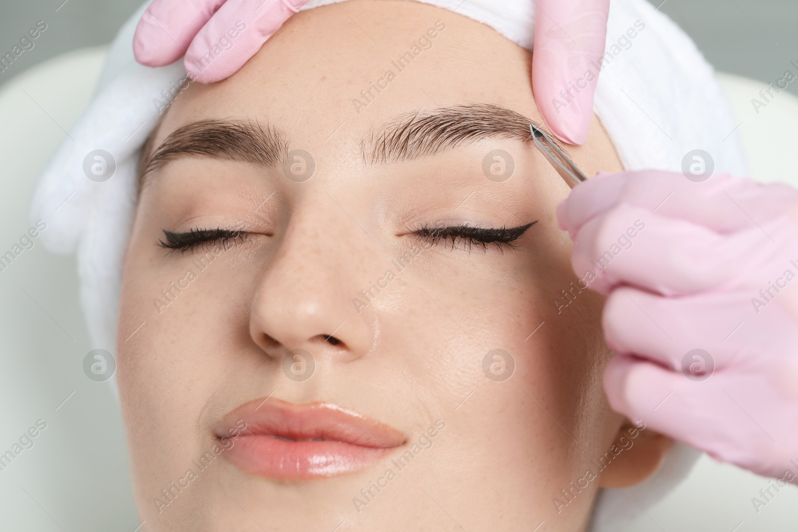 Photo of Beautician plucking young woman's eyebrow in beauty salon, closeup