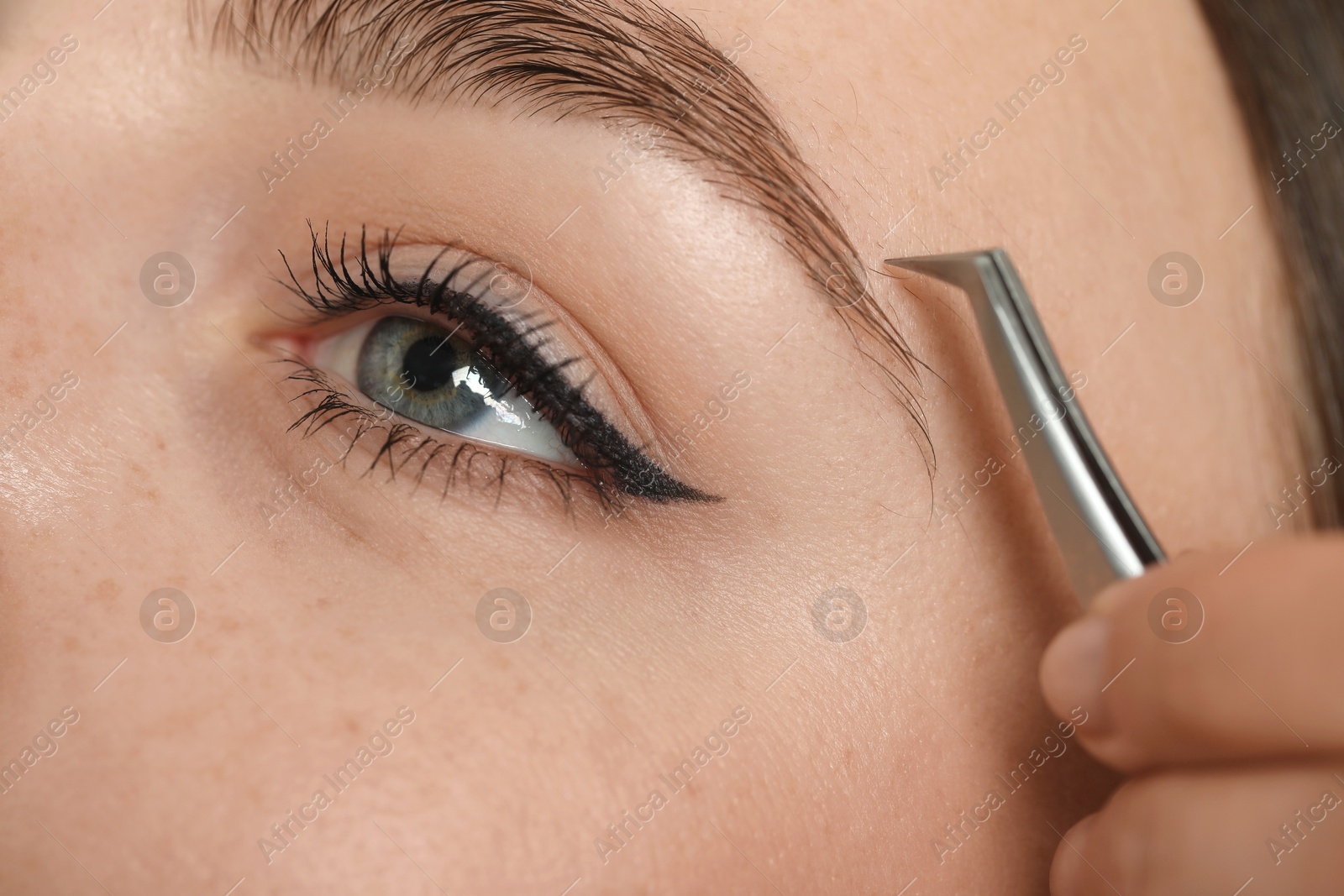 Photo of Beautician plucking young woman's eyebrow, closeup view