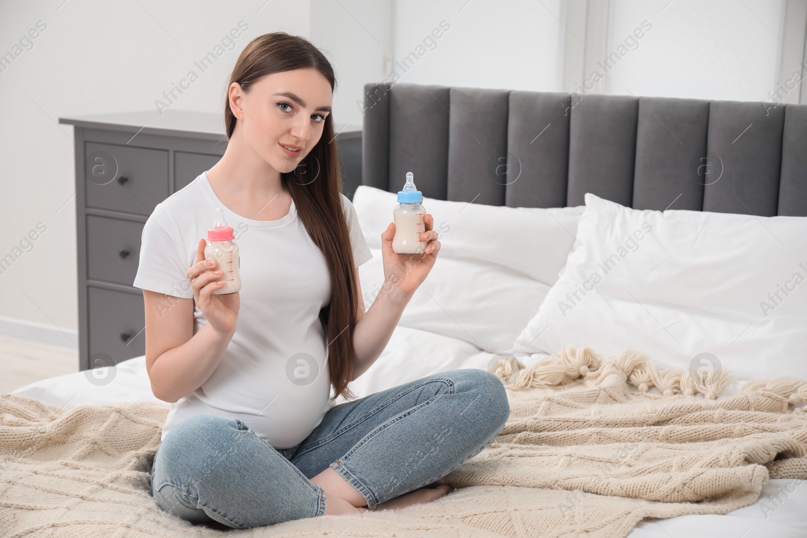 Photo of Expecting twins. Pregnant woman holding two bottles with milk at home, space for text