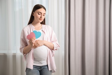 Photo of Expecting twins. Pregnant woman holding two paper cutouts of hearts at home, space for text