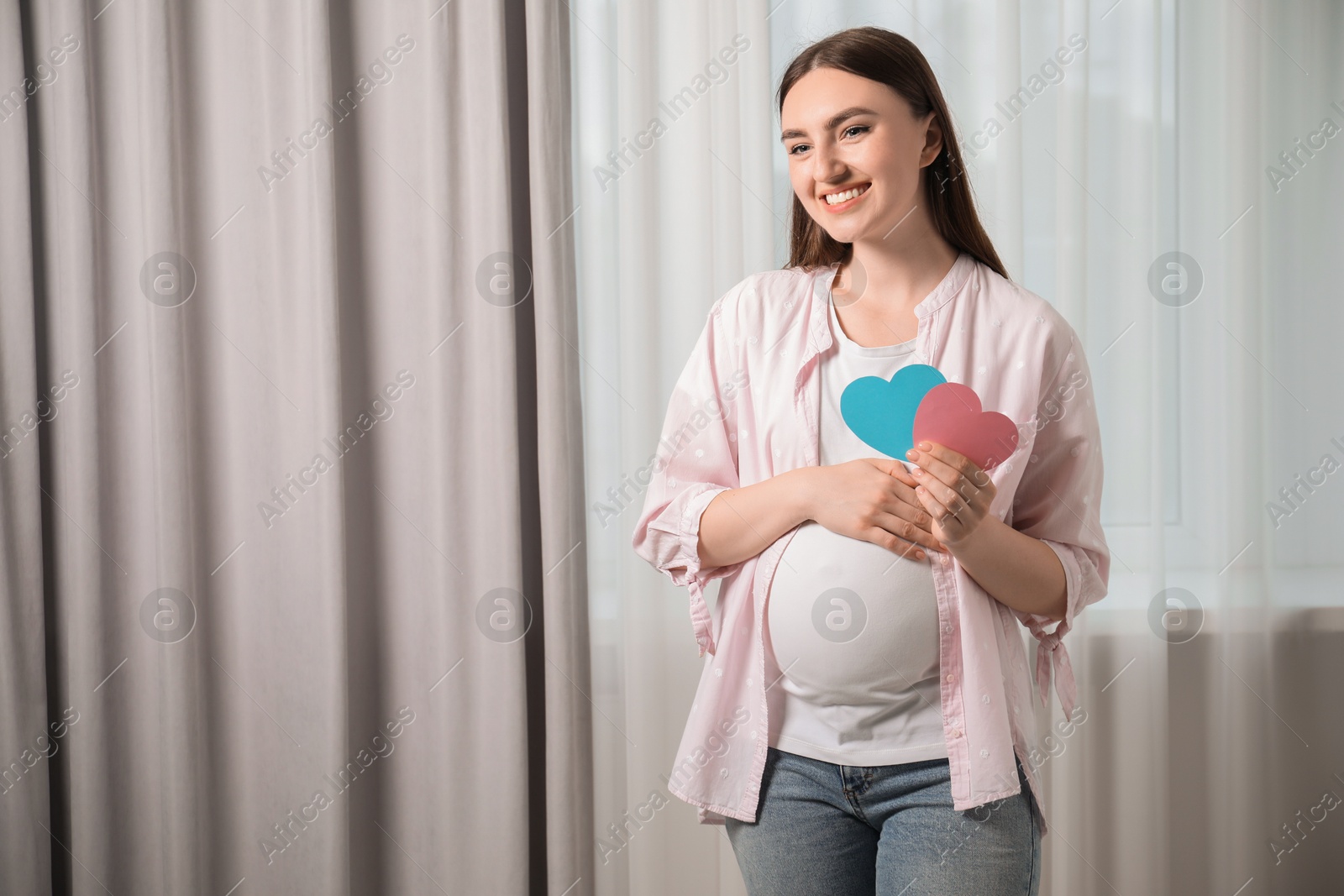 Photo of Expecting twins. Pregnant woman holding two paper cutouts of hearts at home, space for text