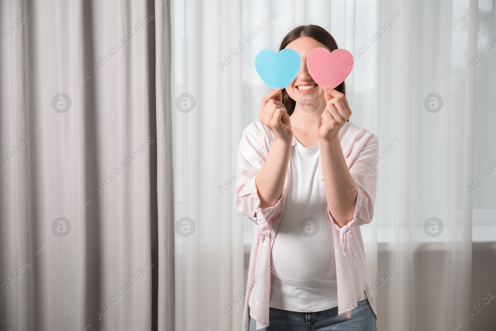 Photo of Expecting twins. Pregnant woman holding two paper cutouts of hearts at home, space for text