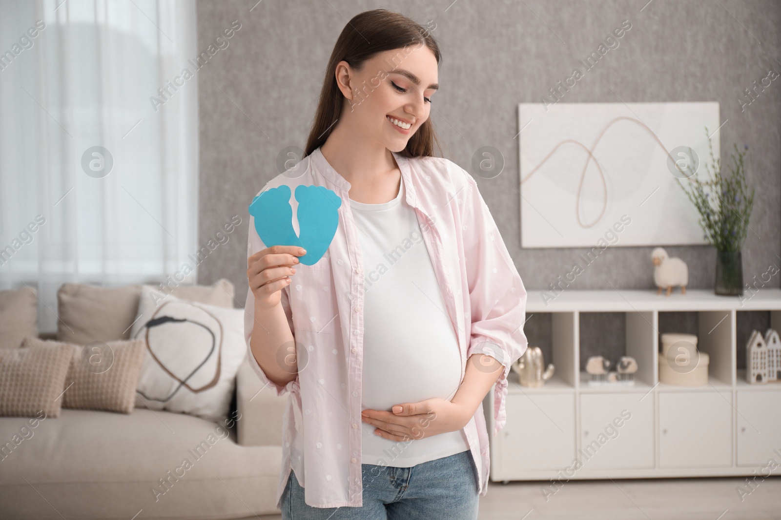 Photo of Expecting twins. Pregnant woman holding two paper cutouts of feet at home