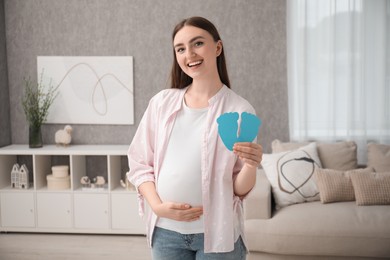 Photo of Expecting twins. Pregnant woman holding two paper cutouts of feet at home
