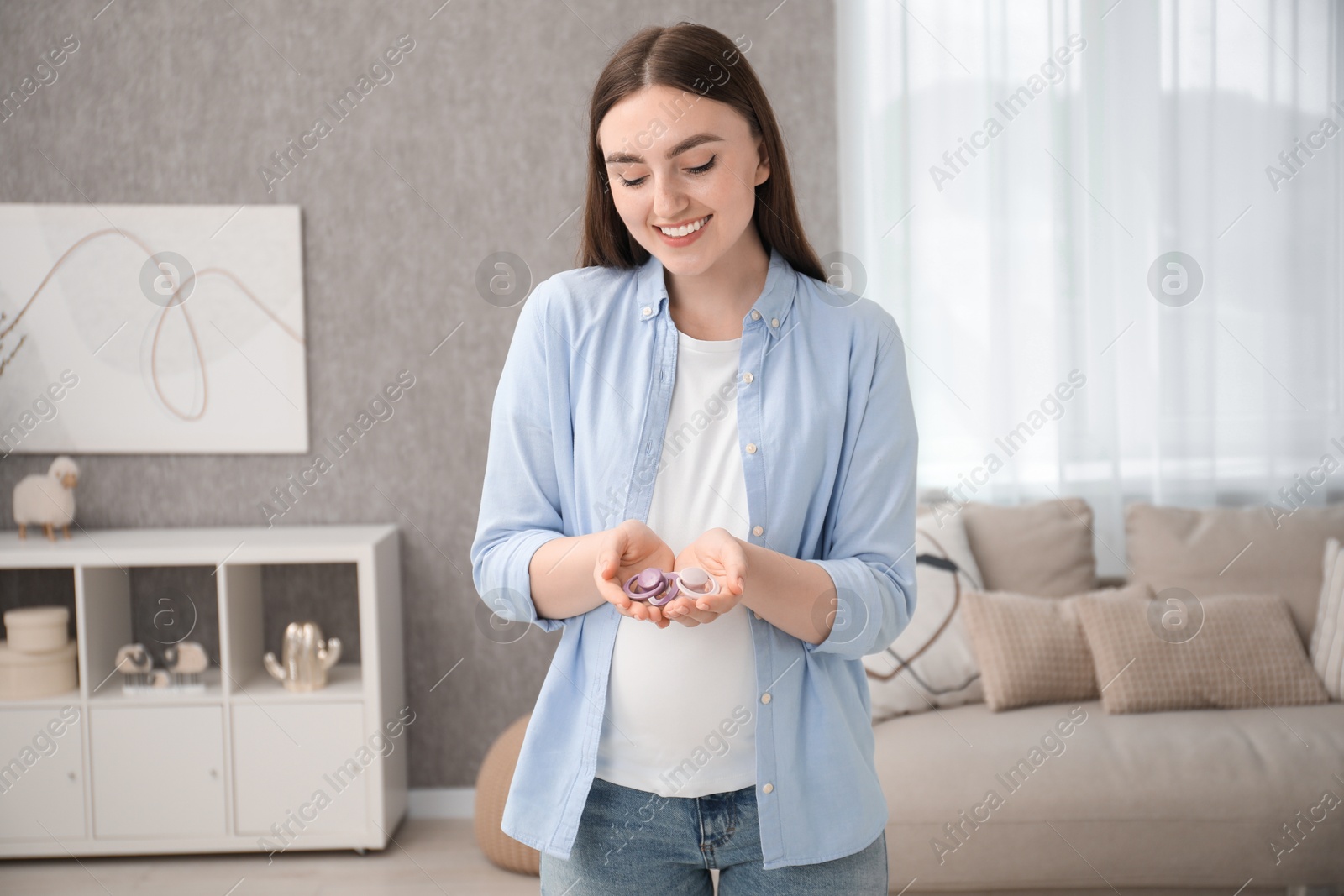 Photo of Expecting twins. Pregnant woman holding two pacifiers at home