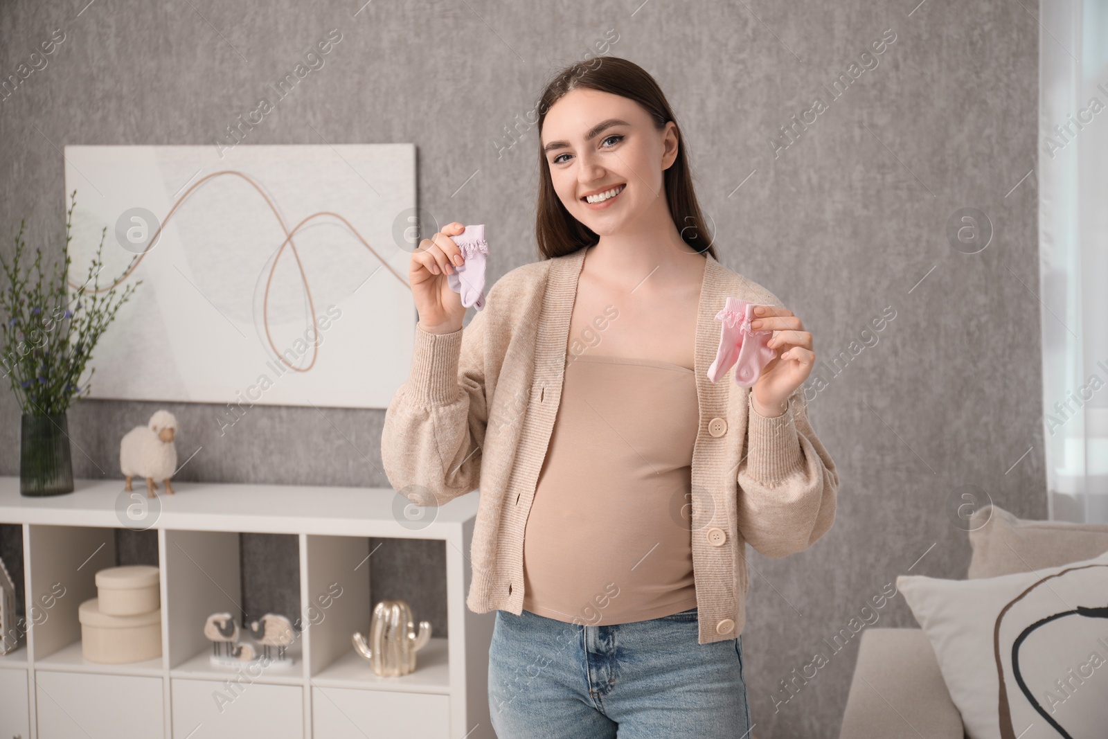 Photo of Expecting twins. Pregnant woman holding two pairs of socks at home