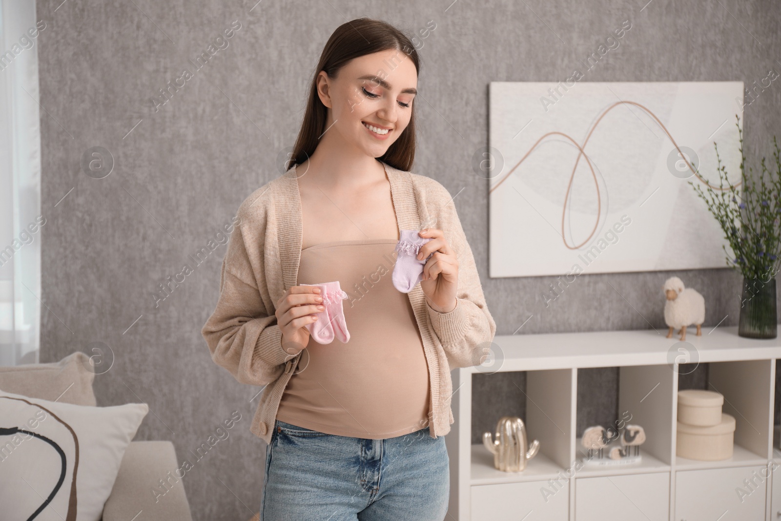 Photo of Expecting twins. Pregnant woman holding two pairs of socks at home