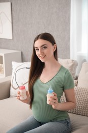 Photo of Expecting twins. Pregnant woman holding two bottles of milk at home