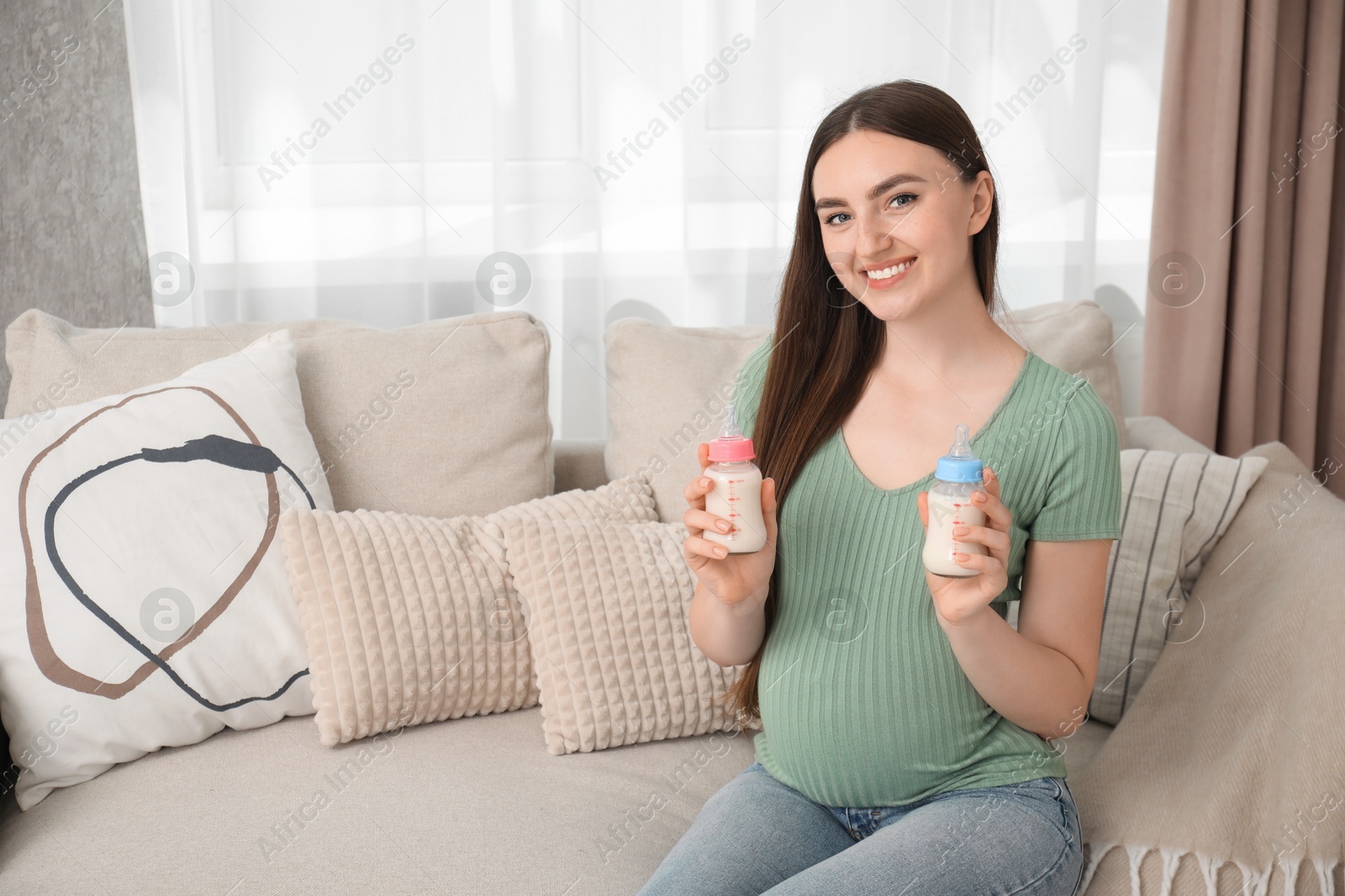 Photo of Expecting twins. Pregnant woman holding two bottles of milk at home, space for text