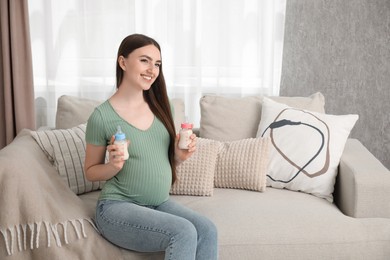 Photo of Expecting twins. Pregnant woman holding two bottles of milk at home, space for text
