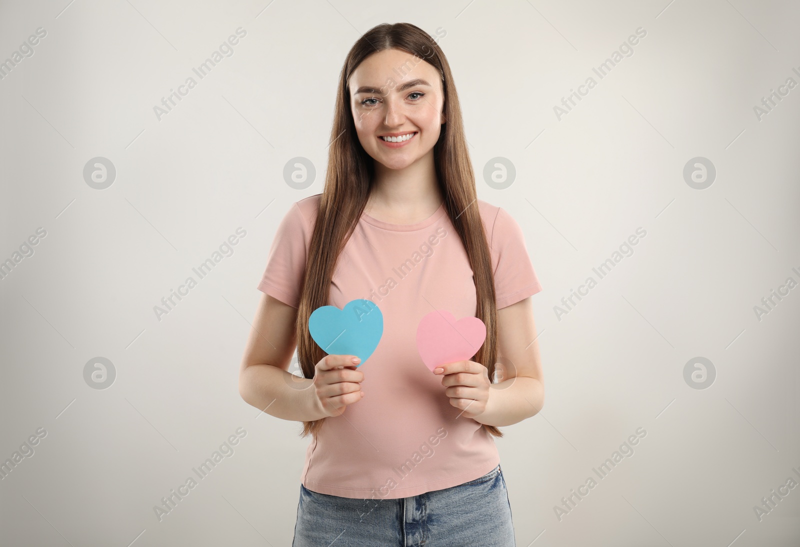 Photo of Expecting twins. Pregnant woman holding two paper cutouts of hearts on light grey background